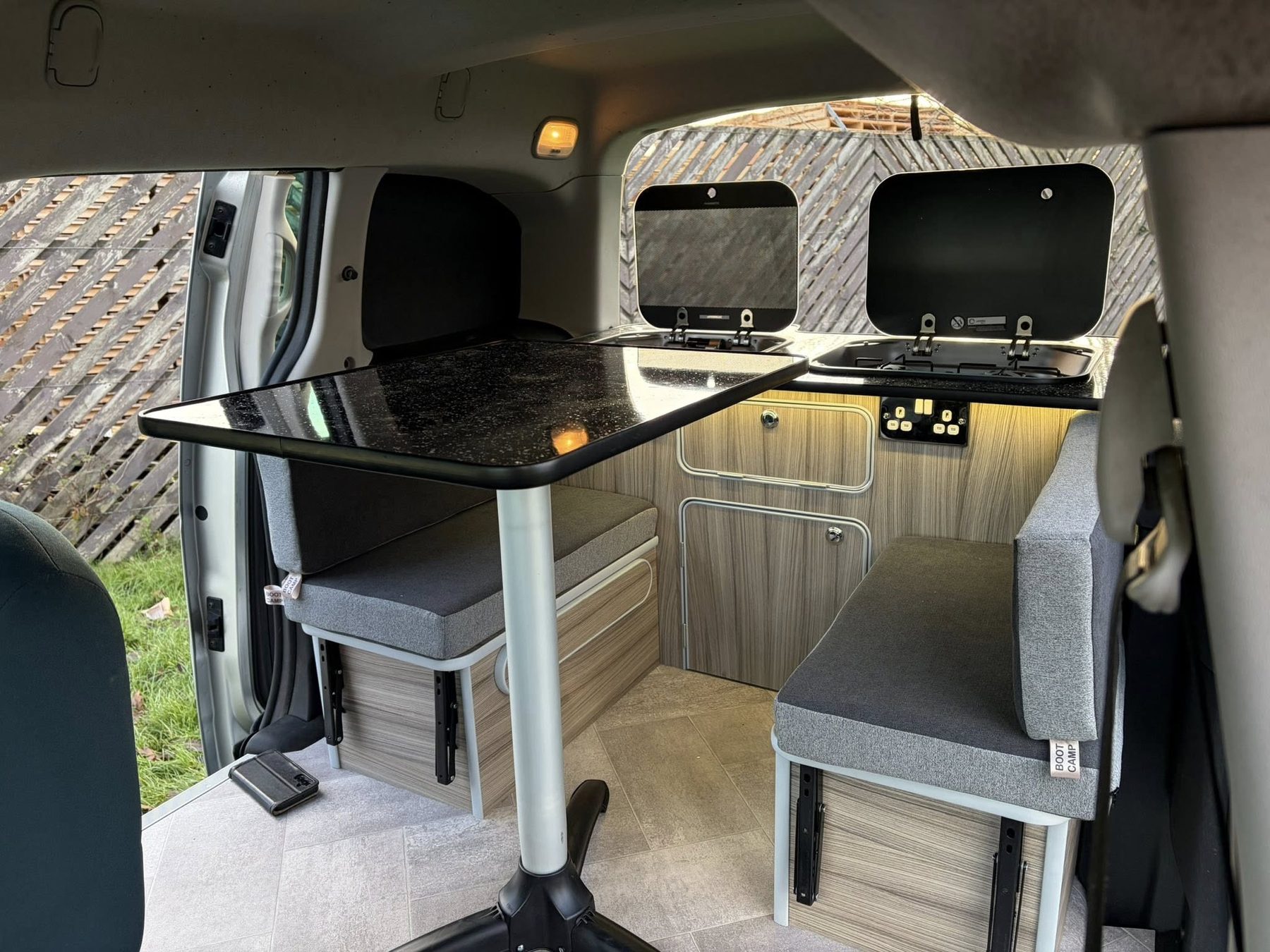 Wood-effect cabinets, grey cushions and a pedestal table in a Boot Camp Campers interior.