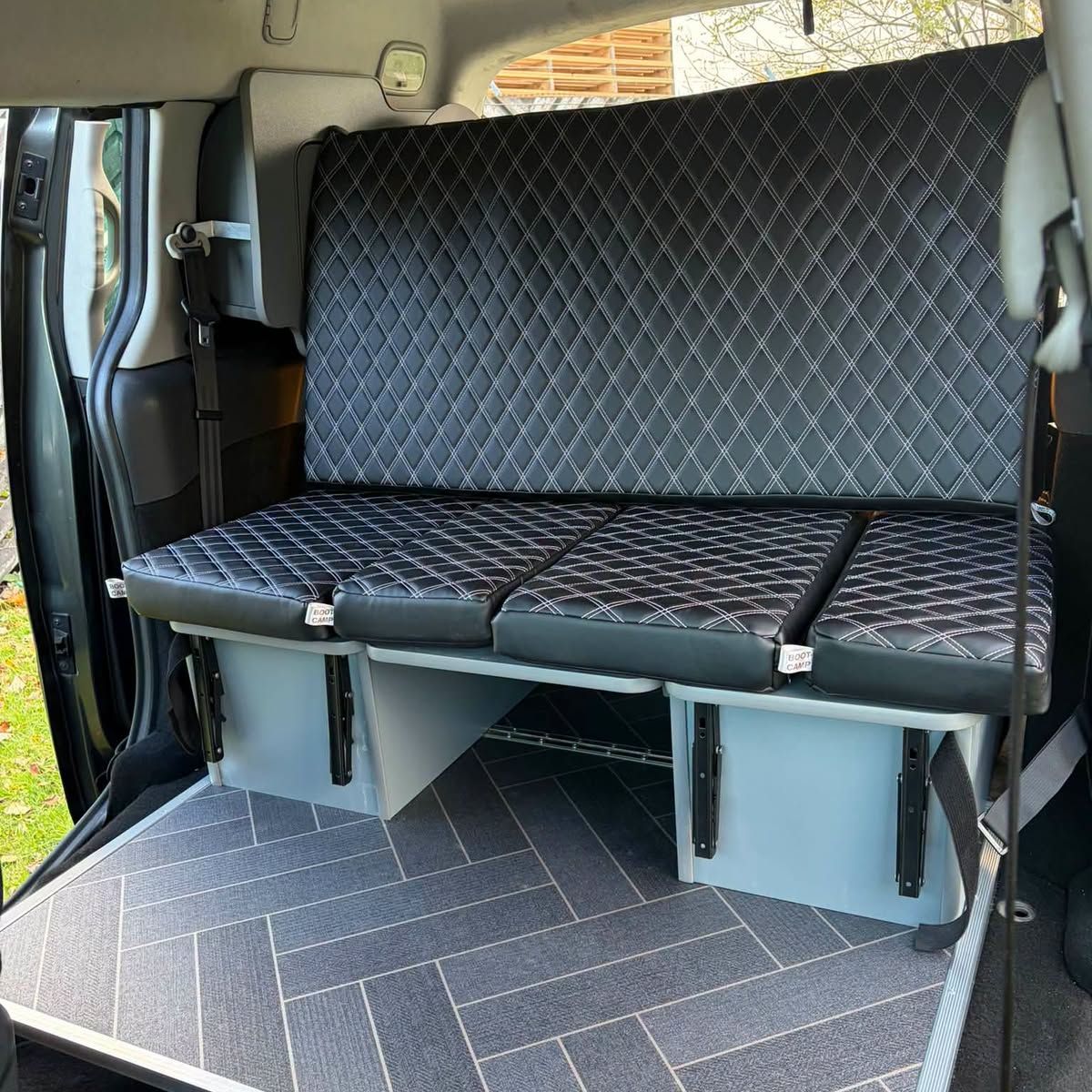 Quilted rear bench over grey storage, photographed from the open back doors.
